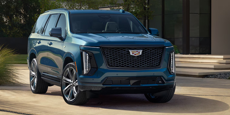 Blue Cadillac Escalade SUV parked in a modern setting with greenery and a building in the background.
