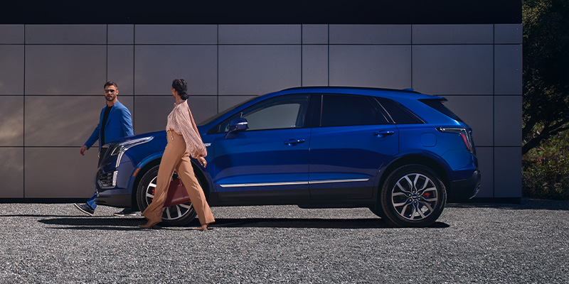 A man and woman walking next to a blue luxury XT5 in a modern outdoor setting.