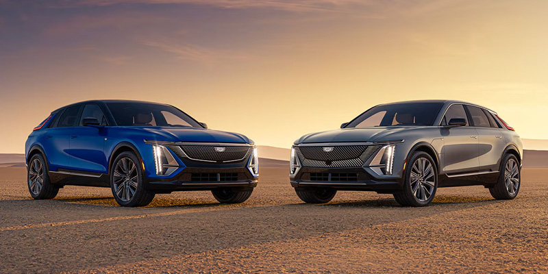 Two Cadillac SUVs parked in a vast desert landscape under a clear blue sky.
